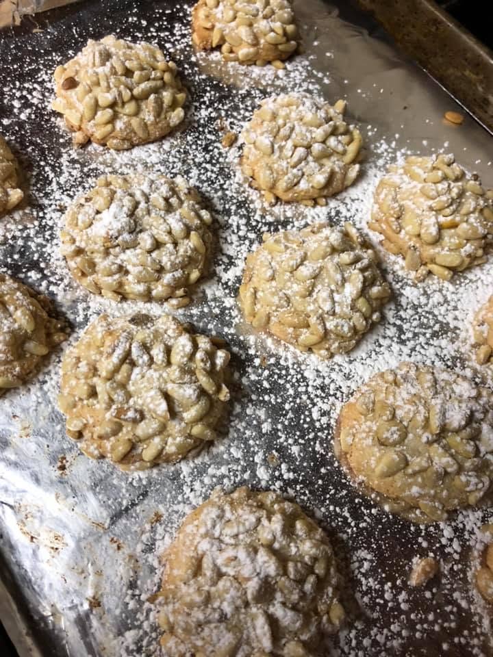finished golden pignoli cookies dusted with powdered sugar on a baking sheet