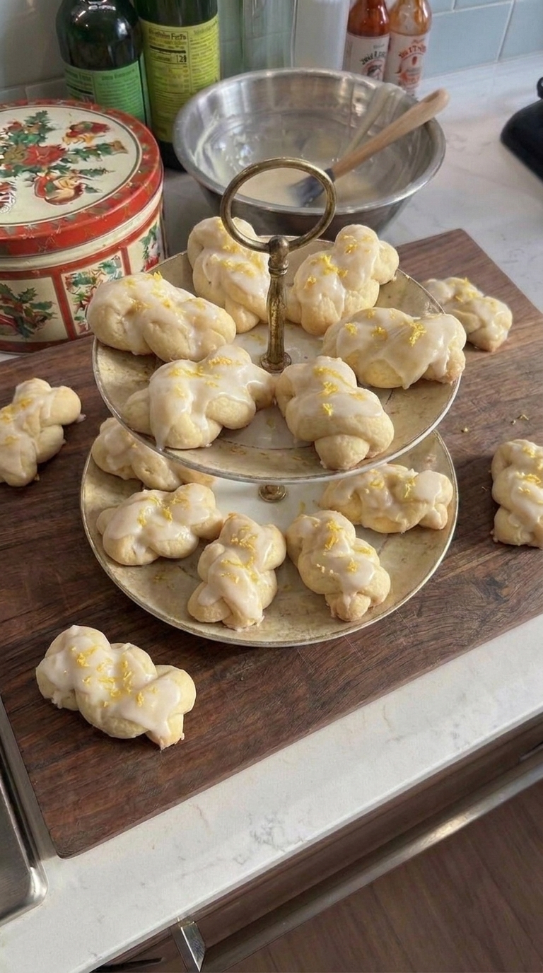 Homemade Italian lemon knot cookies topped with white lemon glaze and fresh lemon zest on a vintage two-tier serving stand.