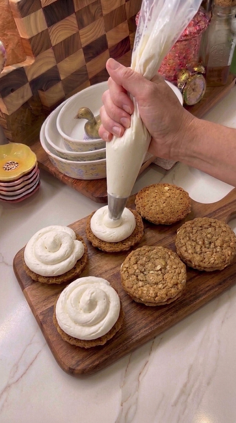 Piping fluffy marshmallow cream filling onto homemade oatmeal cookies to make oatmeal cream pies