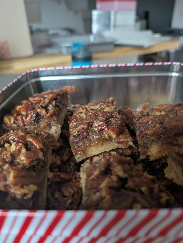 Homemade pecan pie bars with buttery shortbread crust and gooey pecan topping stacked on a wooden cutting board.