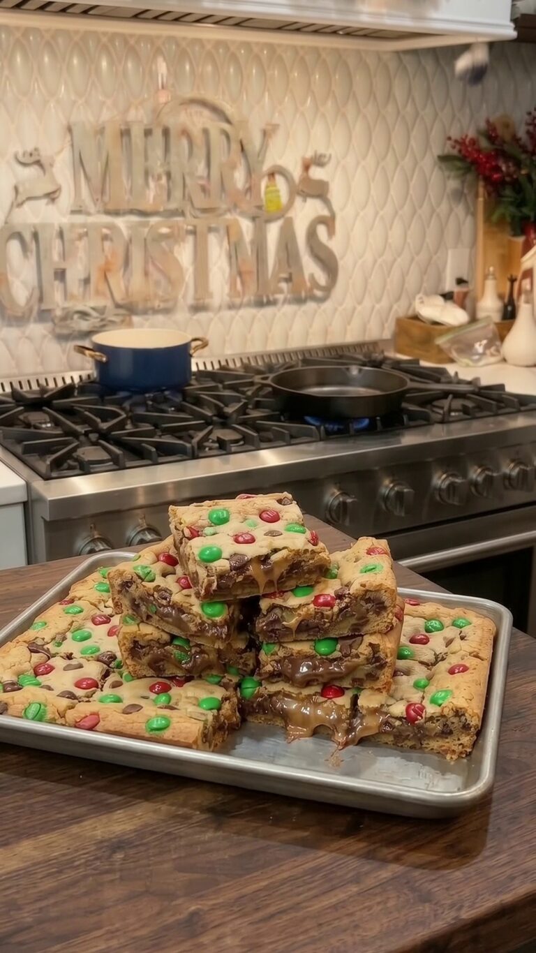 Thick and chewy Christmas cookie bars stacked on a baking sheet with holiday M&Ms and melted chocolate.