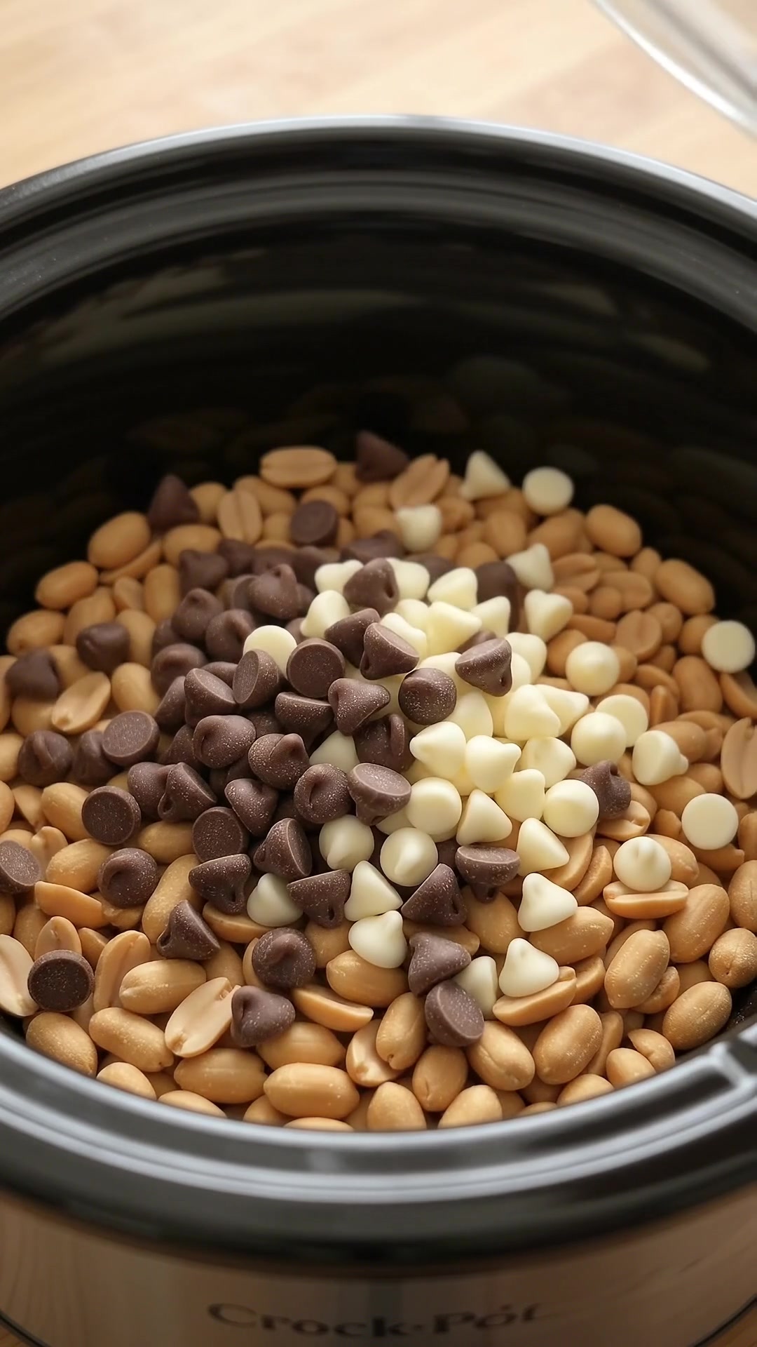 Roasted peanuts and chocolate chips layered inside a slow cooker for homemade Crock Pot candy.