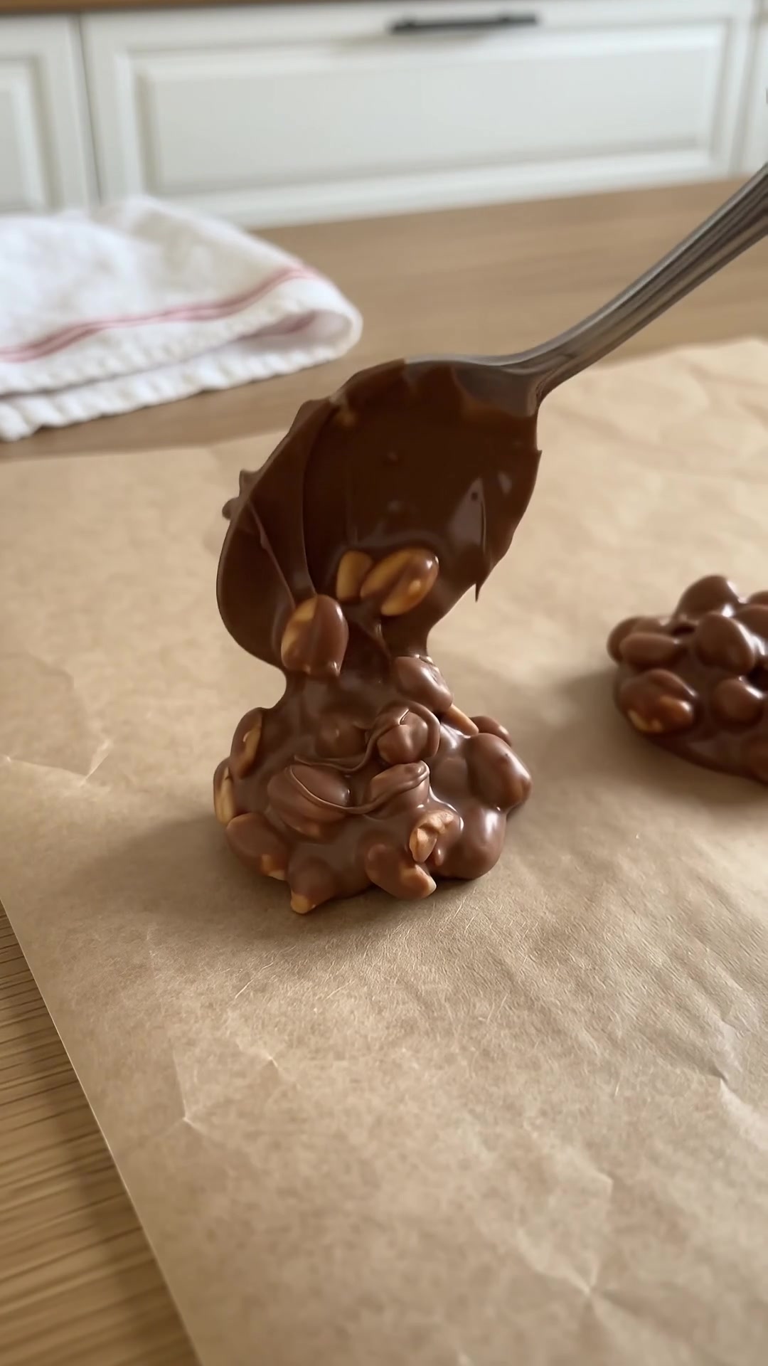 Spoon dropping melted chocolate peanut clusters onto parchment paper to make homemade Crock Pot candy.