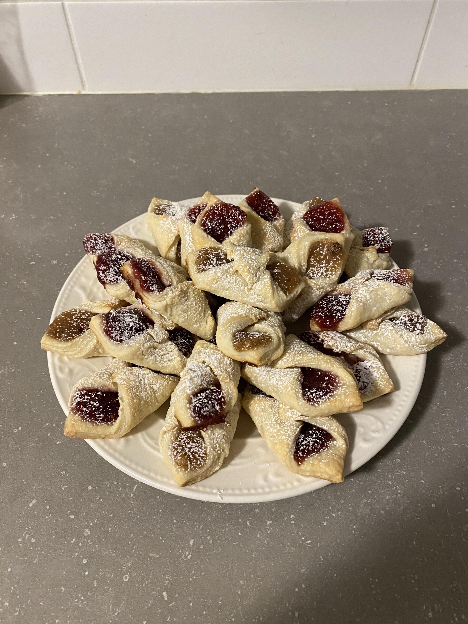 omemade Polish Kołaczki cookies with red raspberry and golden apricot preserves on a white serving plate