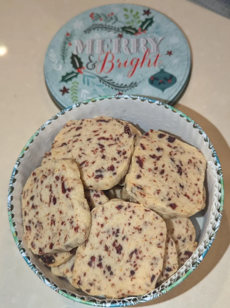 Round cranberry orange pistachio shortbread cookies with red cranberries and green pistachios on a holiday cookie tray