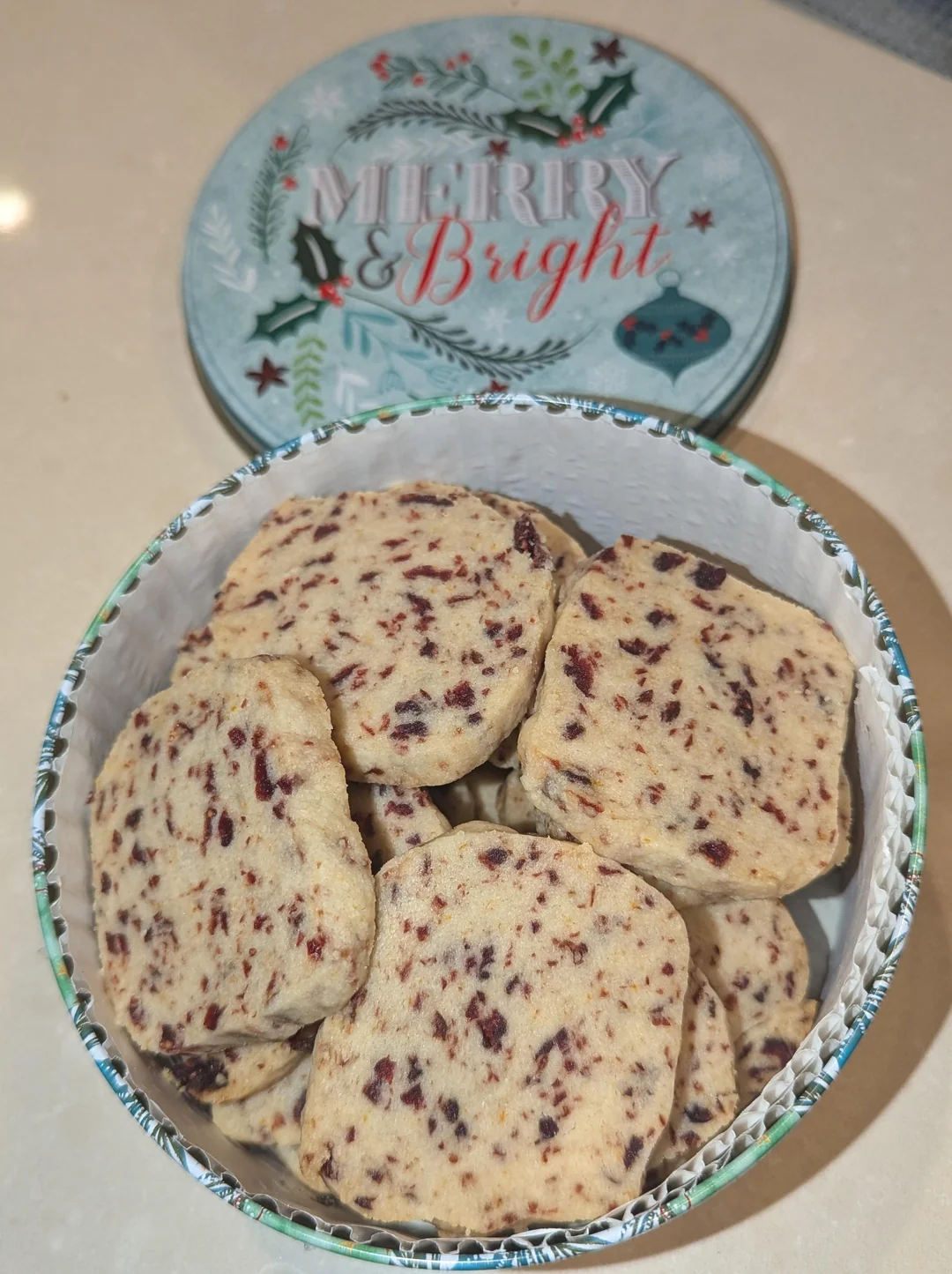 Round cranberry orange pistachio shortbread cookies with red cranberries and green pistachios on a holiday cookie tray