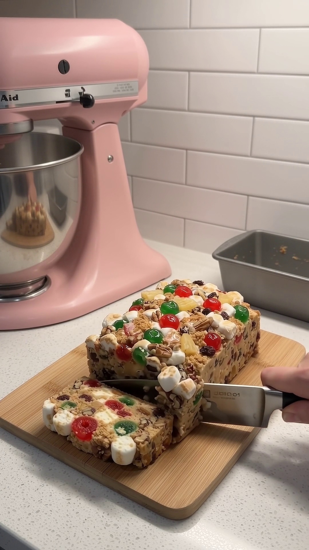 Homemade no-bake icebox fruitcake being sliced on a wooden cutting board, showing colorful candied fruit and marshmallows.