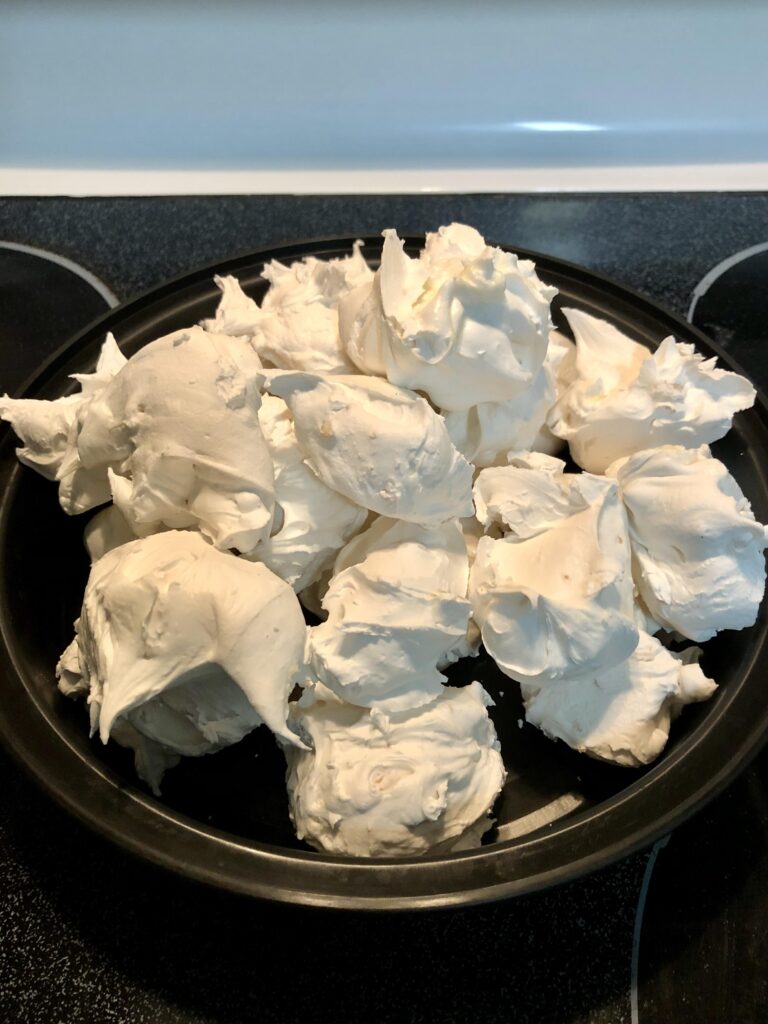 Homemade old-fashioned white divinity candy with fluffy swirled tops and pecan halves arranged on a Christmas candy tray.