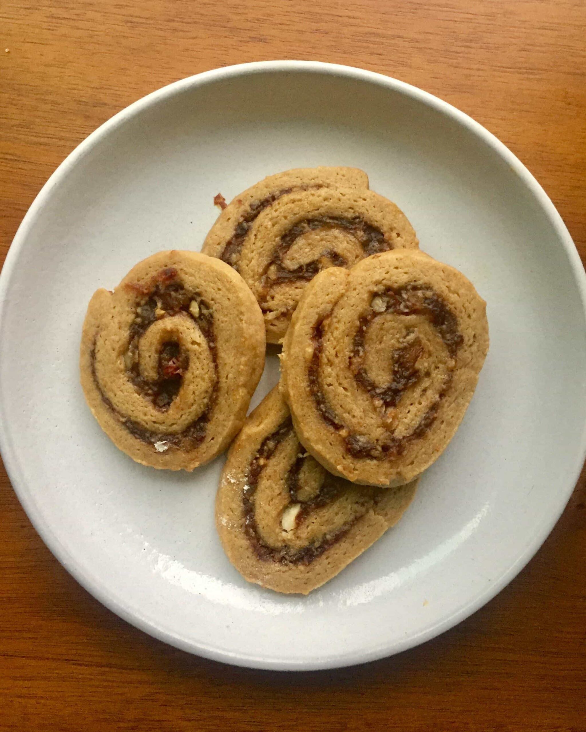 Old-fashioned date pinwheel cookies with golden buttery edges and dark date filling spirals arranged on a vintage Christmas cookie plate.