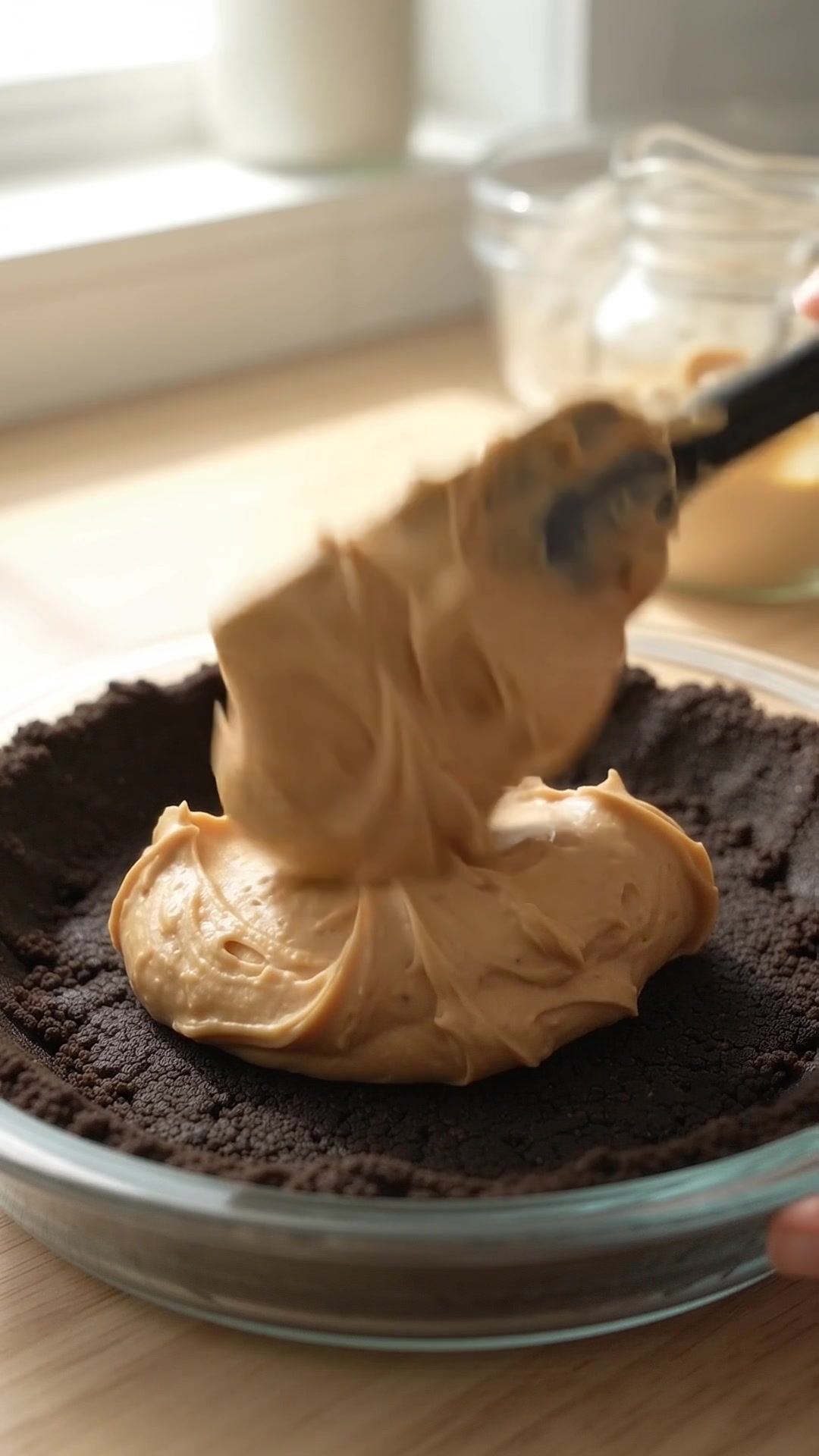 Fluffy peanut butter cream filling being added to a chocolate Oreo crust for no-bake peanut butter pie.