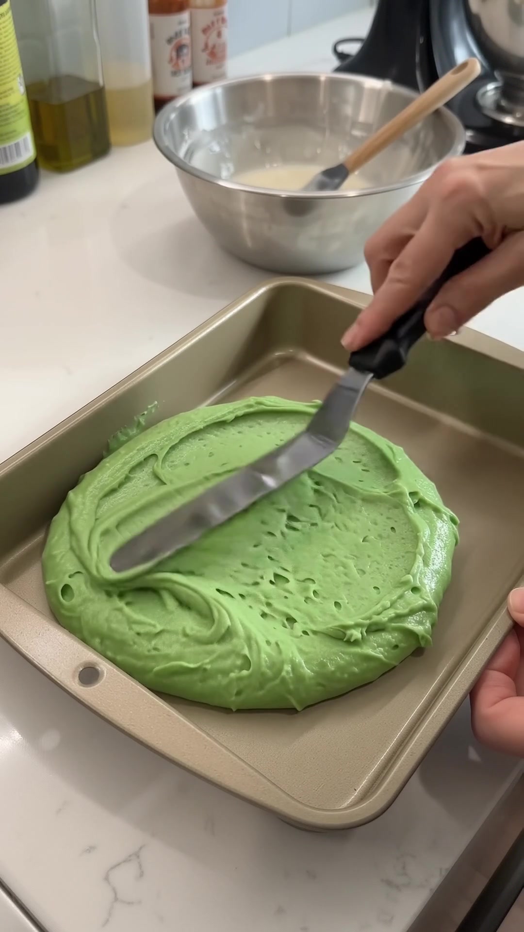 Spreading green almond cake batter into a baking pan for homemade Italian rainbow cookies.