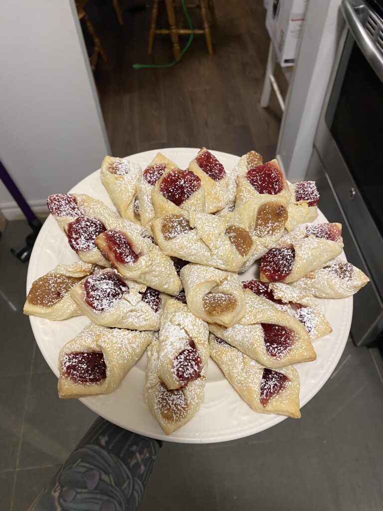 Traditional Polish Kołaczki cream cheese cookies filled with raspberry and apricot jam and dusted with powdered sugar.