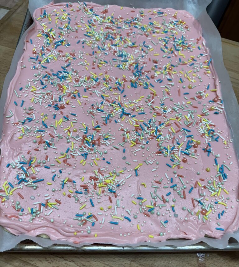Pink buttercream frosting spread over soft sugar cookie bars in a baking pan