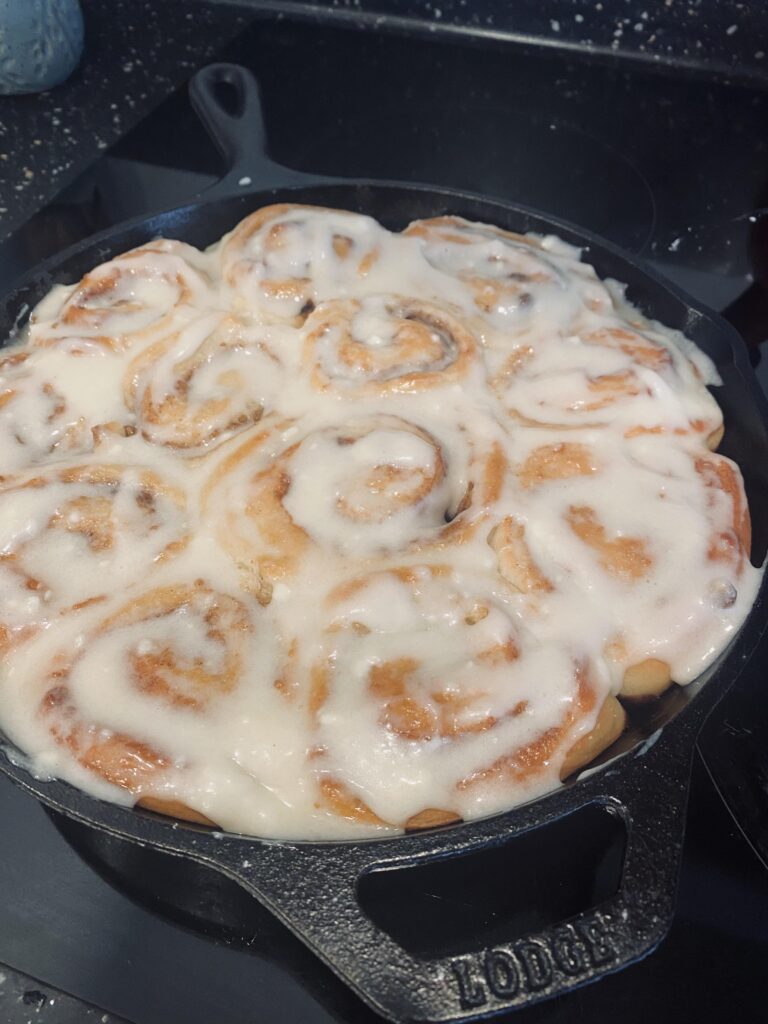 Homemade cinnamon rolls baked in a Lodge cast iron skillet and covered with thick cream cheese glaze.