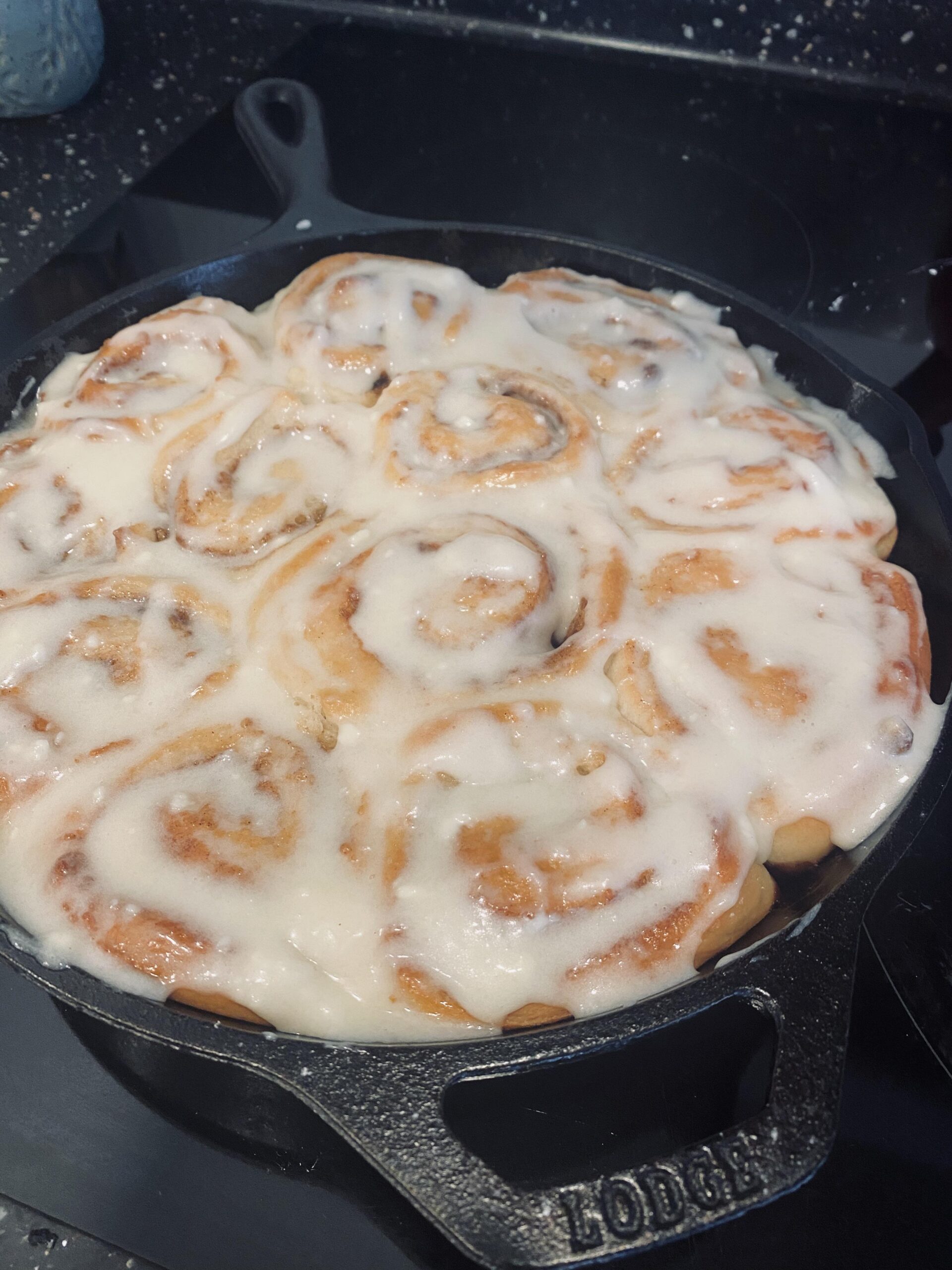 Homemade cinnamon rolls baked in a Lodge cast iron skillet and covered with thick cream cheese glaze.